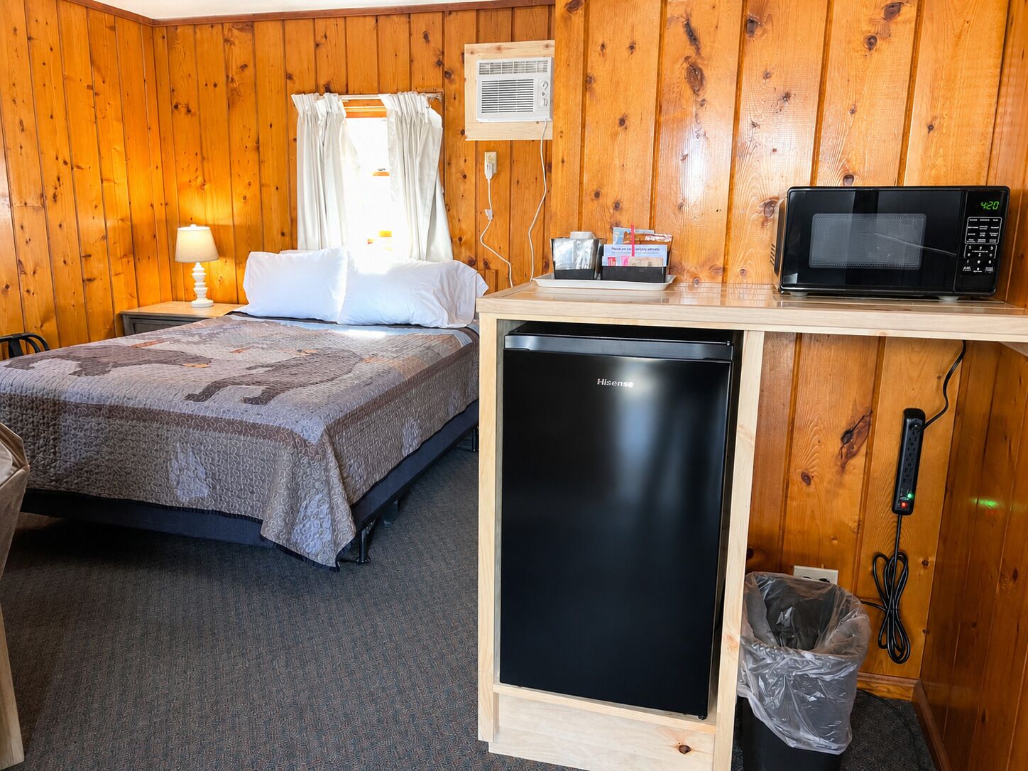A room with a bed, a microwave, a small refrigerator, and a trash bin.