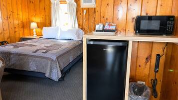 A room with a bed, a microwave, a small refrigerator, and a trash bin.