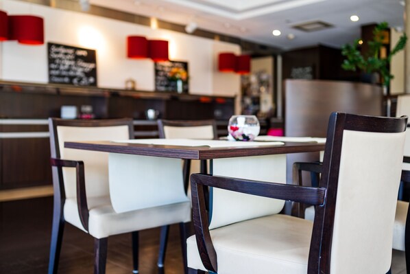 Un interior de restaurante moderno con mesas y sillas de madera, un panel con la carta y una planta al fondo.