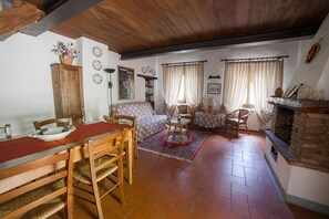 Un salon chaleureux avec une cheminée, un coin repas avec une table et des chaises en bois, et un tapis à motifs.
