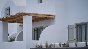 Un edificio blanco con una pérgola de madera, ventanas arqueadas y pequeñas plantas en la base.