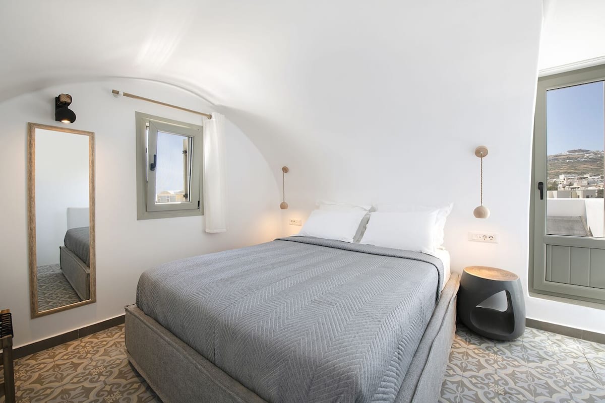 Un dormitorio con cama, un espejo grande, una ventana y vista a la ciudad.