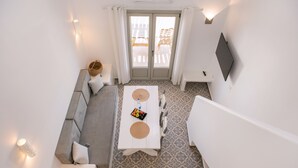 Una habitación moderna con sofá, una mesa de comedor con individuales, televisor montado en la pared y suelo estampado.