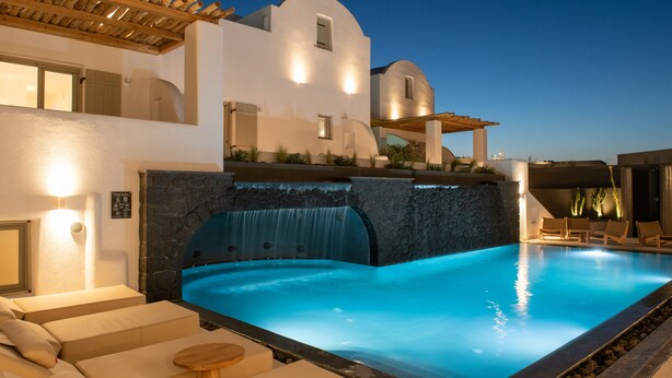 Una piscina con cascada, sillas de descanso y un edificio blanco de diseño moderno.