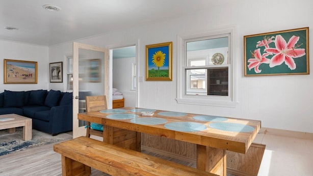 A dining area with a wooden table and benches, white walls, and various framed artworks.