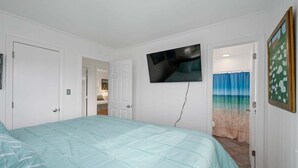 A bedroom with a bed, a television mounted on the wall, and a door leading to another room.