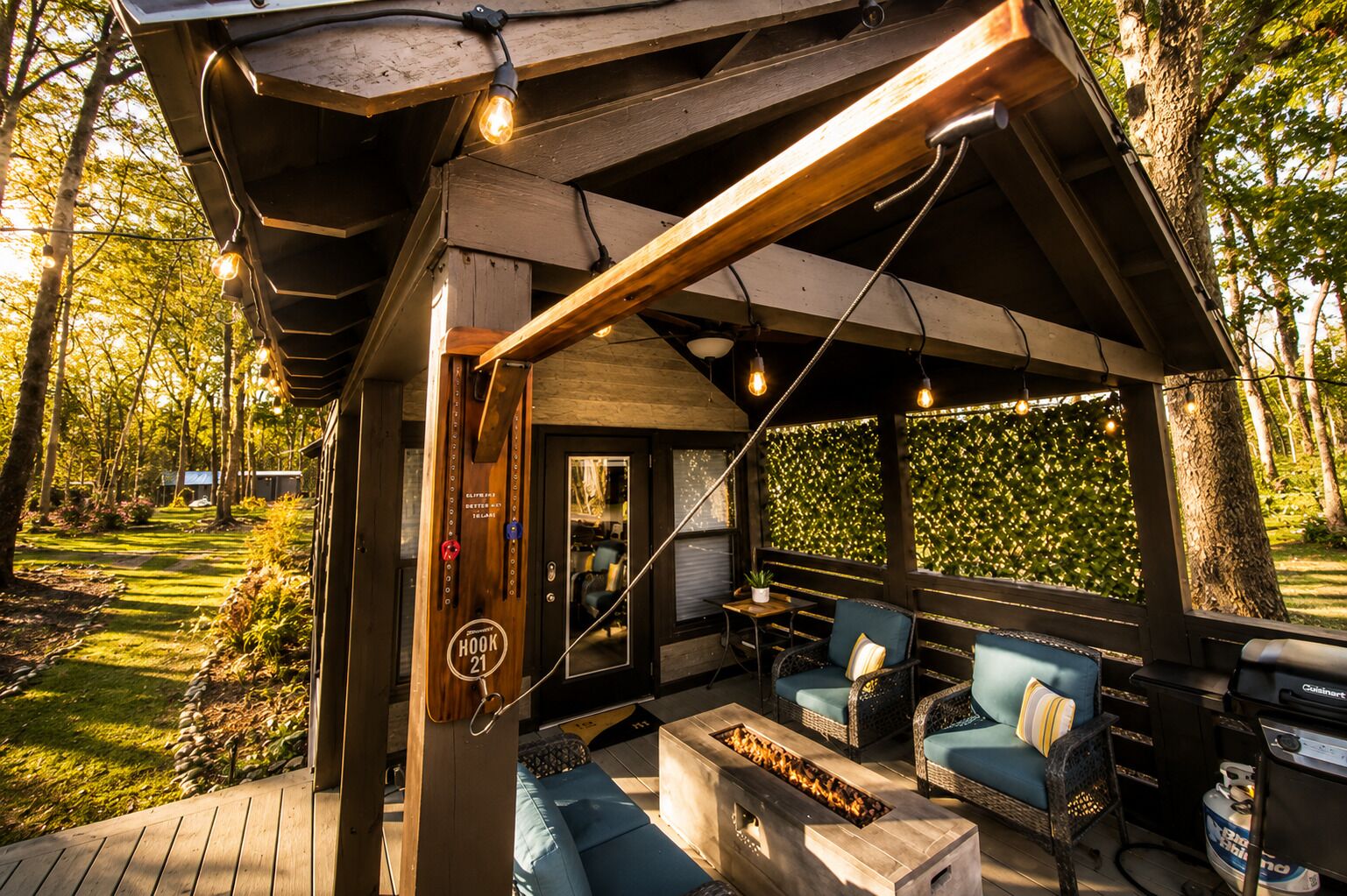 An outdoor patio with wooden furniture, a fire pit, and string lights.