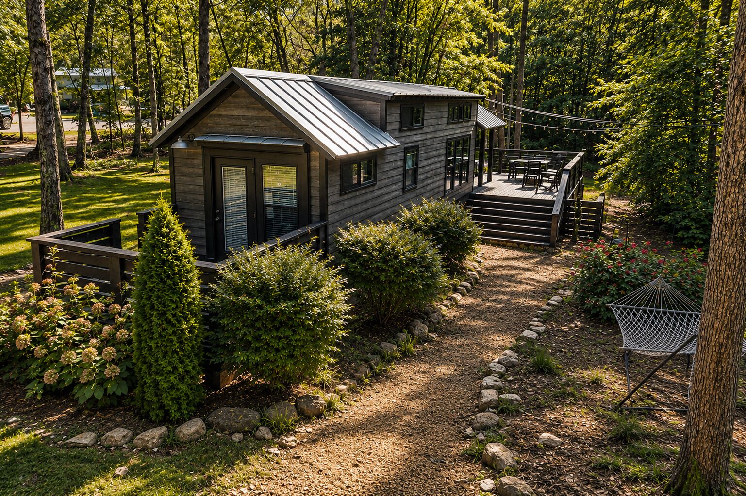 A cabin with a deck, surrounded by a garden with various plants and a gravel path.