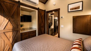 Un dormitorio con una cama grande, un armario, aire acondicionado integrado, una zona de cocina y un cuadro en la pared.