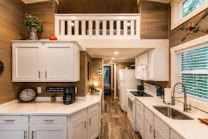 A modern kitchen with white cabinetry, a coffee machine, and a clock on the wall. - Edgewater at The Retreat at Water's Edge (Tracy City)