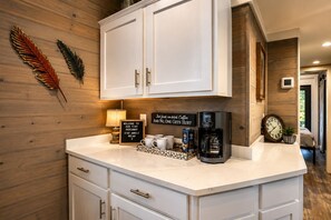 A kitchen with white cabinets, a coffee machine, and a sign that reads 'Welcome to our tiny hideaway stay awhile relax.' - Edgewater at The Retreat at Water's Edge (Tracy City)