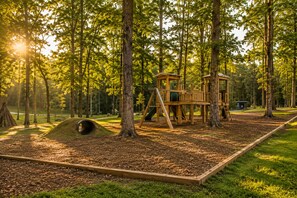 A playground with a wooden play structure, surrounded by trees and a grassy area.