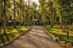 A gravel pathway leading to a lodge surrounded by tall trees. - Edgewater at The Retreat at Water's Edge (Tracy City)