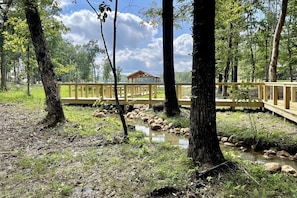 Una terraza de madera con un pabellón en un área boscosa con un arroyo.