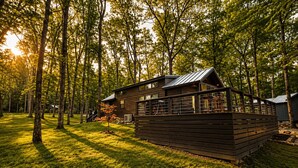 A cabin with a deck, surrounded by trees and grass. - Edgewater at The Retreat at Water's Edge (Tracy City)