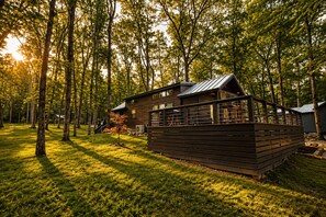 A cabin with a deck, surrounded by trees and grass. - Edgewater at The Retreat at Water's Edge (Tracy City)