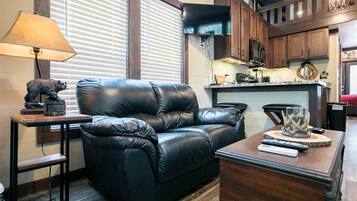 A living room with a black leather sofa, a small table with a lamp, and a kitchen area in the background.
