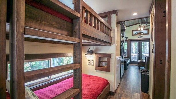 A bunk bed room with a red bedspread, wooden beams, and a hallway leading to a dining area. - Jenny's Retreat at The Retreat at Deer Lick Falls (Monteagle)