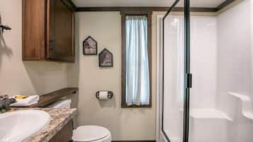 Ein Badezimmer mit Toilette, Waschbecken, Dusche und einem Fenster mit Vorhängen.