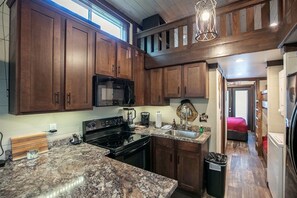 Une cuisine avec des meubles en bois, un micro-ondes noir, une cuisinière, des plans de travail en granit et un luminaire suspendu.