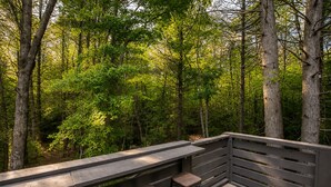 A wooden deck with a railing, two stools, and a bench overlooking a forest. - Jenny's Retreat at The Retreat at Deer Lick Falls (Monteagle)