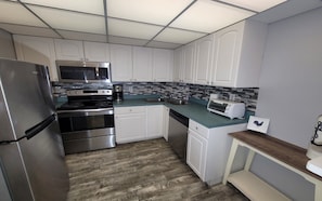 A modern kitchen with stainless steel appliances, white cabinetry, and a tiled backsplash.