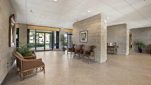 A spacious lobby with a high ceiling, large windows, and a seating area with wicker furniture. - Beachfront 2BR/2BA condo with pool, WiFi, and heated pool access. (Marco Island)