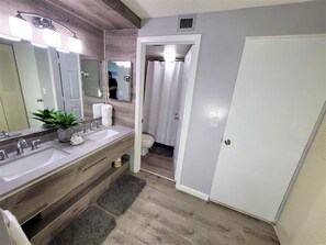 A bathroom with two sinks, a mirror, a shower curtain, and a door. - Beachfront 2BR/2BA condo with pool, WiFi, and heated pool access. (Marco Island)