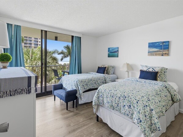 Habitación de hotel con dos camas, un balcón y vistas a palmeras y edificios.