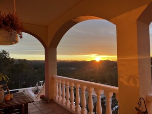 A balcony with a view of the sunset over a hilly landscape.