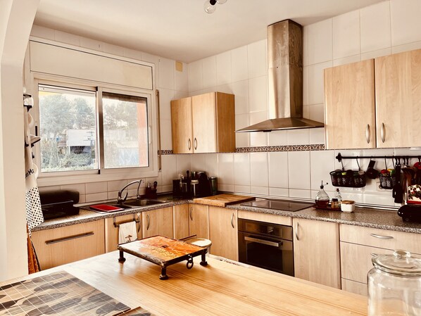 A modern kitchen with wooden cabinets, a stainless steel range hood, and a large window providing natural light.