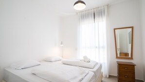 Een nette, goed verlichte slaapkamer met twee bedden, een nachtkastje, een spiegel en een raam met gordijnen.