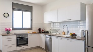 Een moderne keuken met witte kasten, een roestvrijstalen vaatwasser en een raam dat natuurlijk licht binnenlaat.