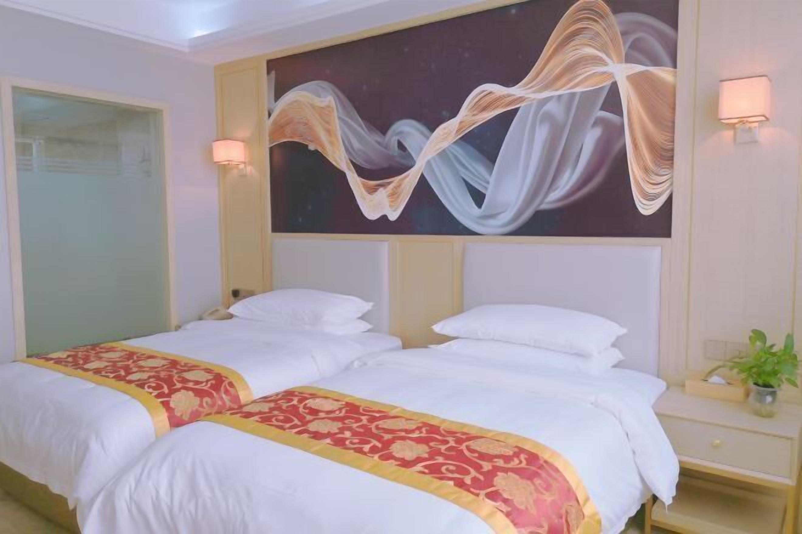 A hotel room with two beds, a large abstract painting on the wall, and a bedside table with a lamp.