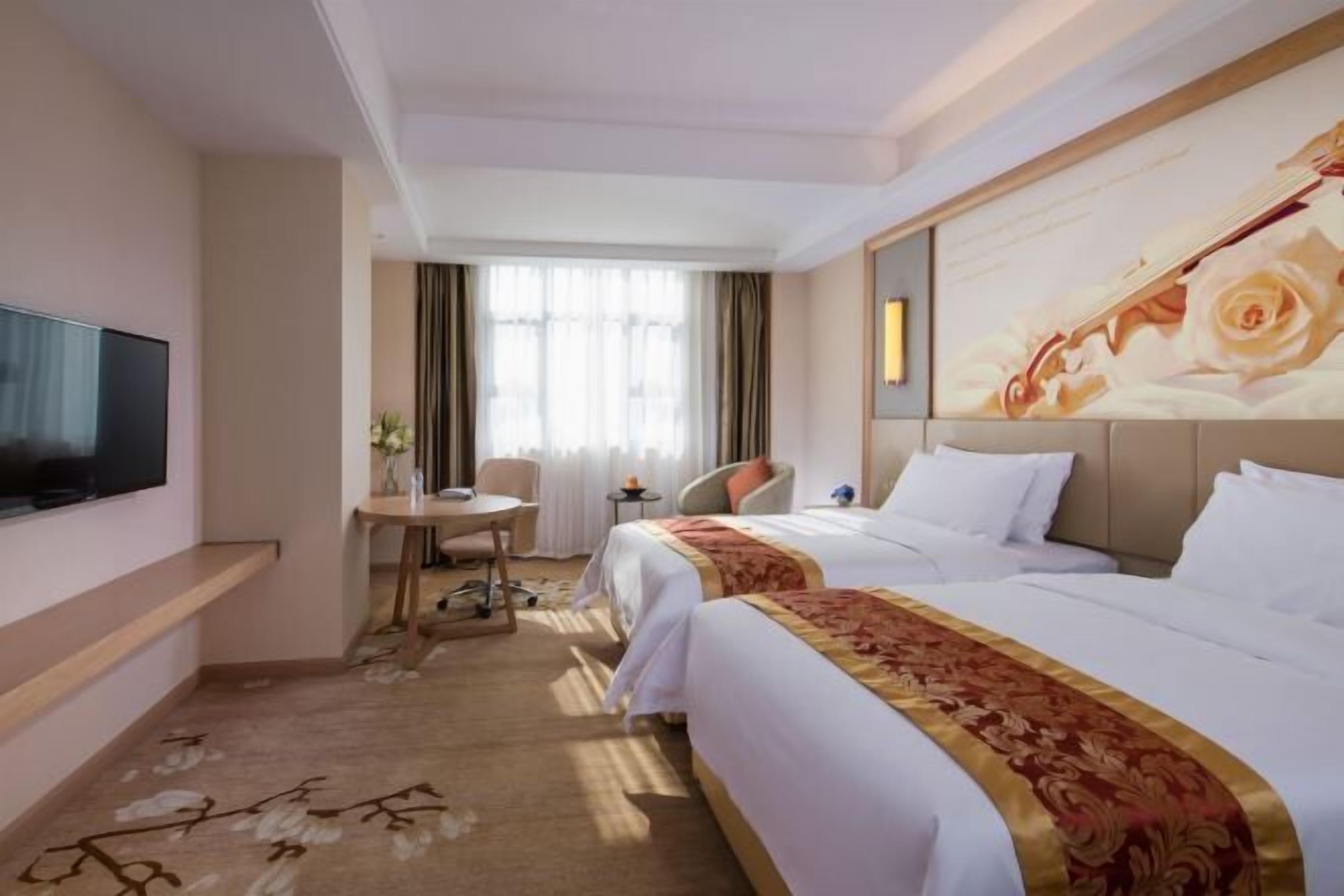 Habitación de hotel con dos camas, un televisor de pantalla plana, un escritorio con silla y un cuadro grande con motivos florales en la pared.