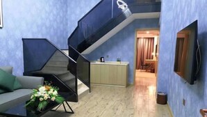 A modern living room with a staircase, a sofa, a coffee table with flowers, and a kitchen area in the background. - Vienna International Hotel (Wenzhou Rui'an Tangxia) (Rui'an)