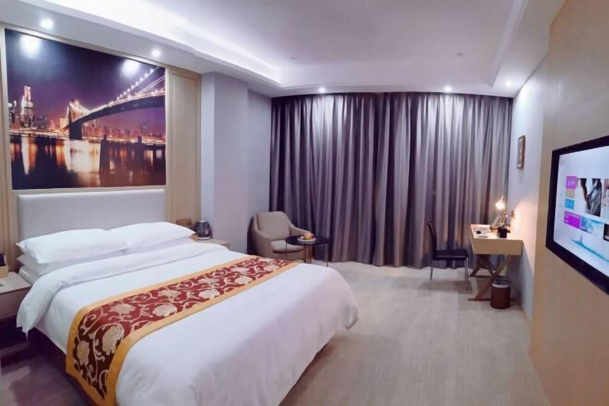 A hotel room with a bed, a desk, a chair, a TV, and a large window with curtains.