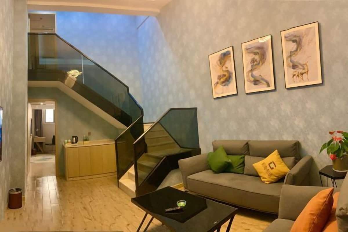 A modern living room with a grey sofa, a coffee table, and a staircase with glass railings.