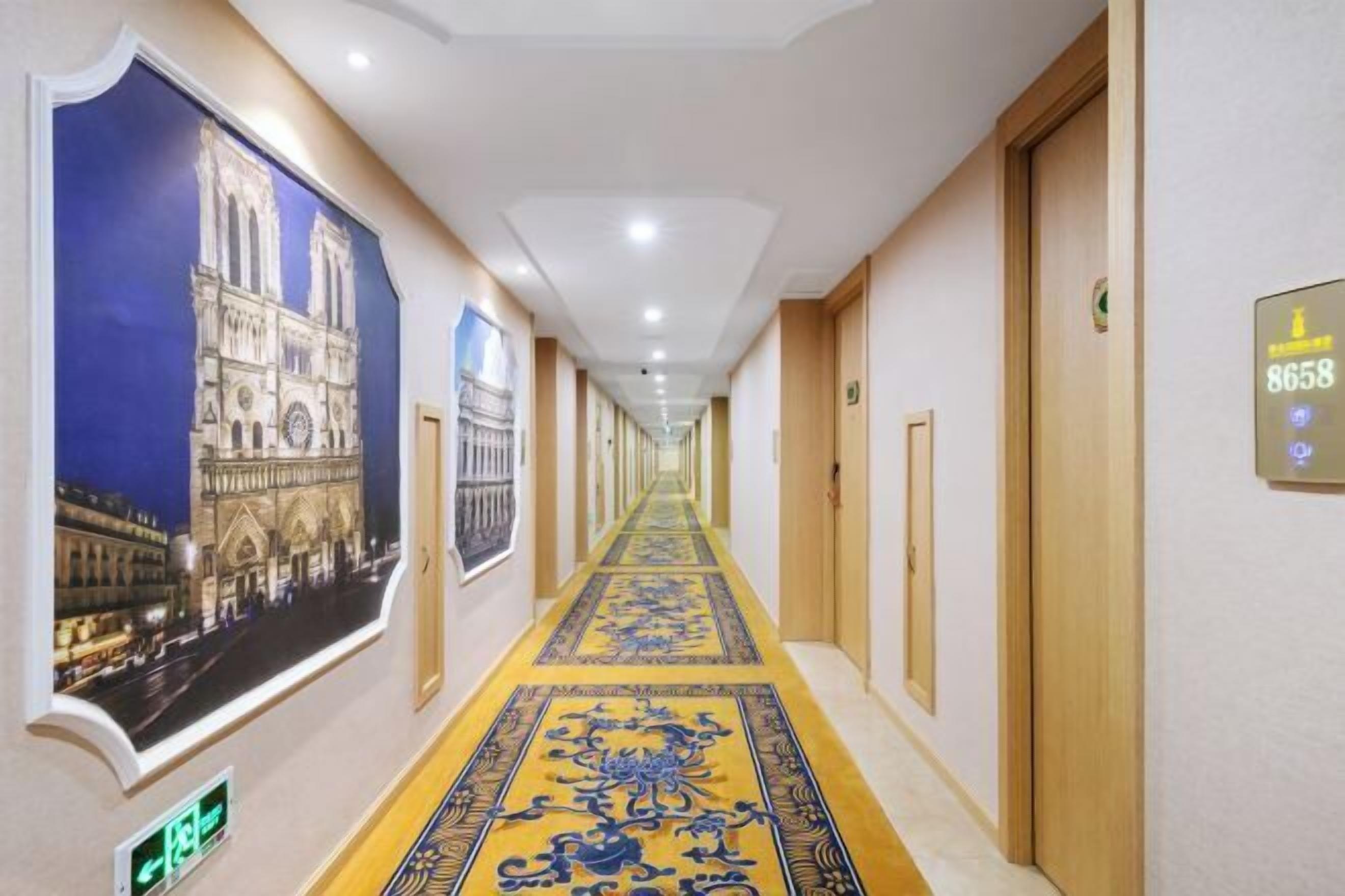 Un couloir d’hôtel avec un long passage, des portes sur la droite et une grande affiche représentant une cathédrale sur la gauche.