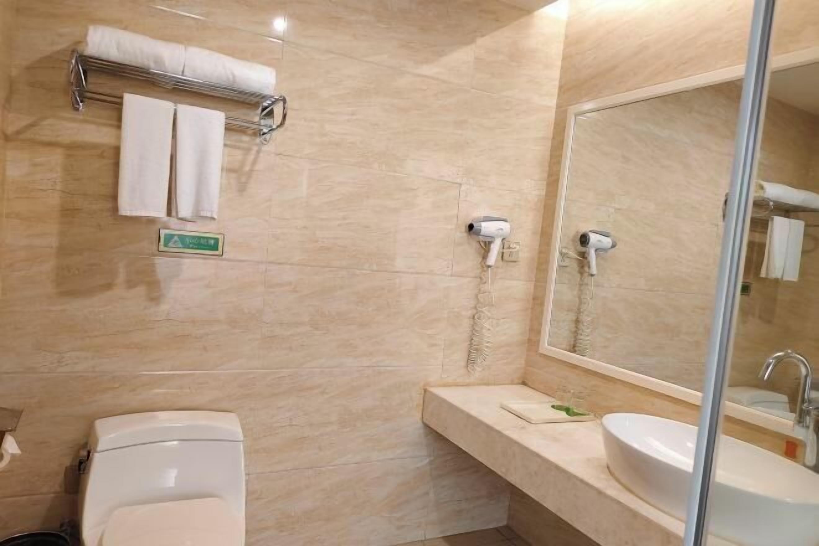 Un baño con inodoro, lavamanos, toallero y espejo.
