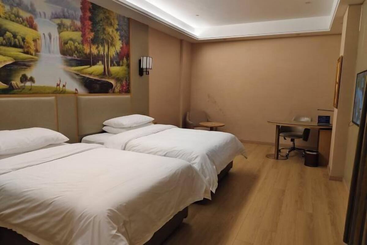 A hotel room with two beds, a desk, a chair, a lamp, and a painting on the wall.
