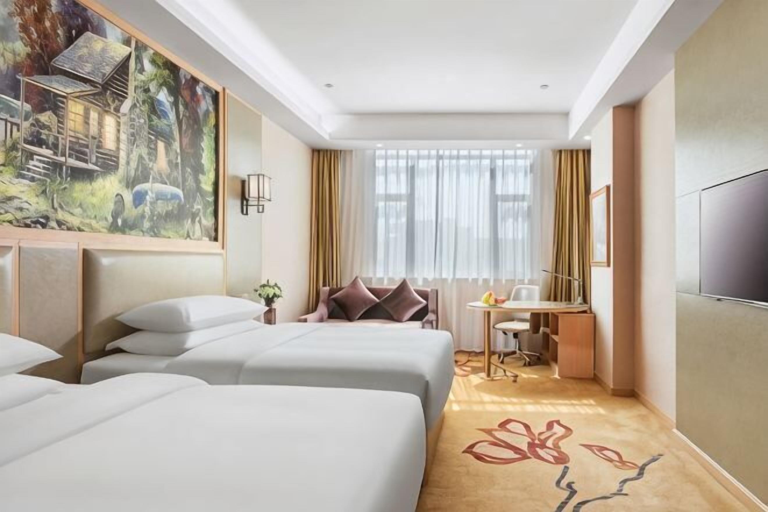 A hotel room with three beds, a desk, a chair, a TV, and a painting on the wall.