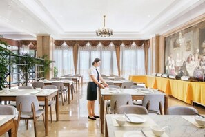 A spacious dining area with multiple tables, a chandelier, and a waiter attending to guests. - Vienna International Hotel (Wenzhou Rui'an Tangxia) (Rui'an)