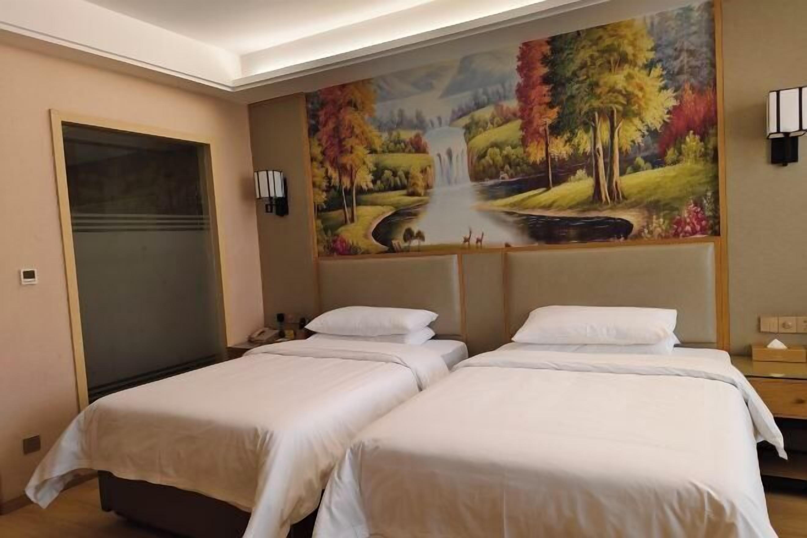 A hotel room with two beds, a large painting of a landscape, and a door.