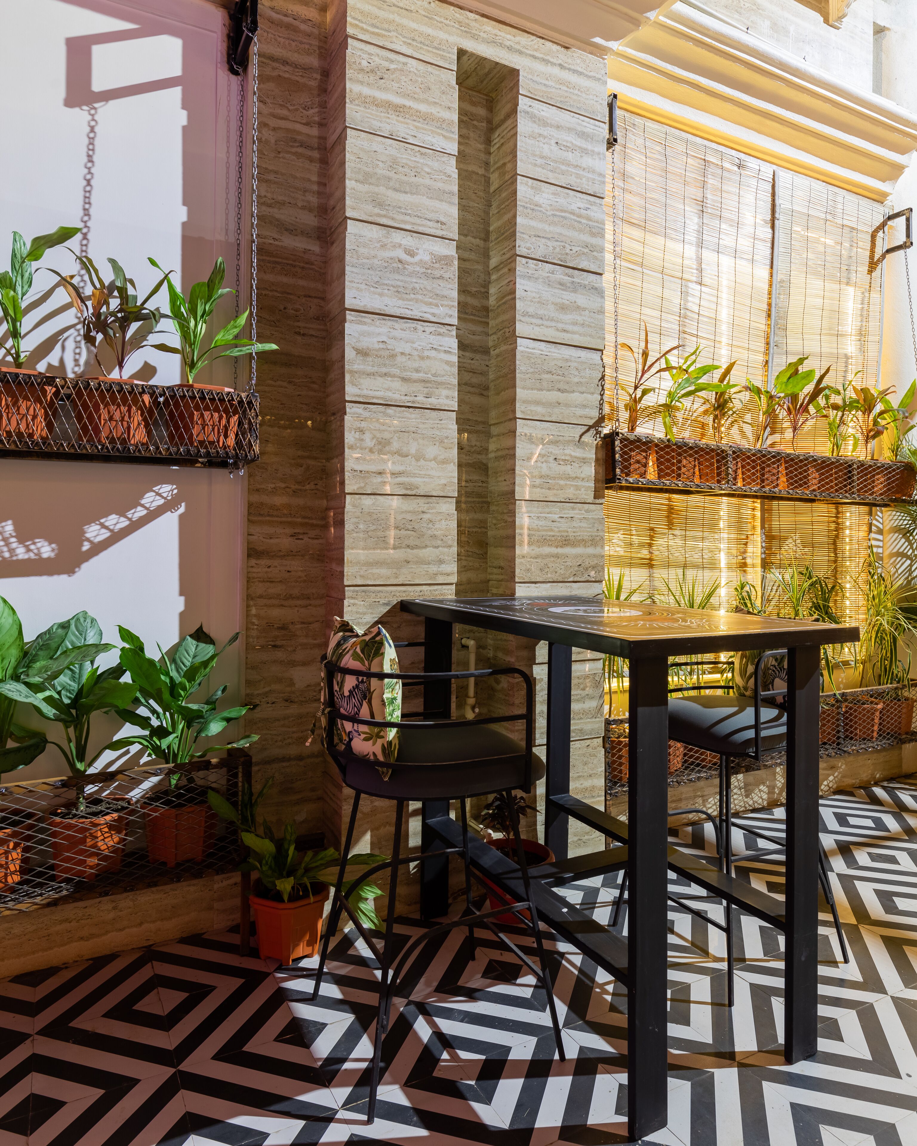 Un espacio moderno al aire libre con una mesa y sillas, rodeado de plantas en macetas y un suelo con diseño.