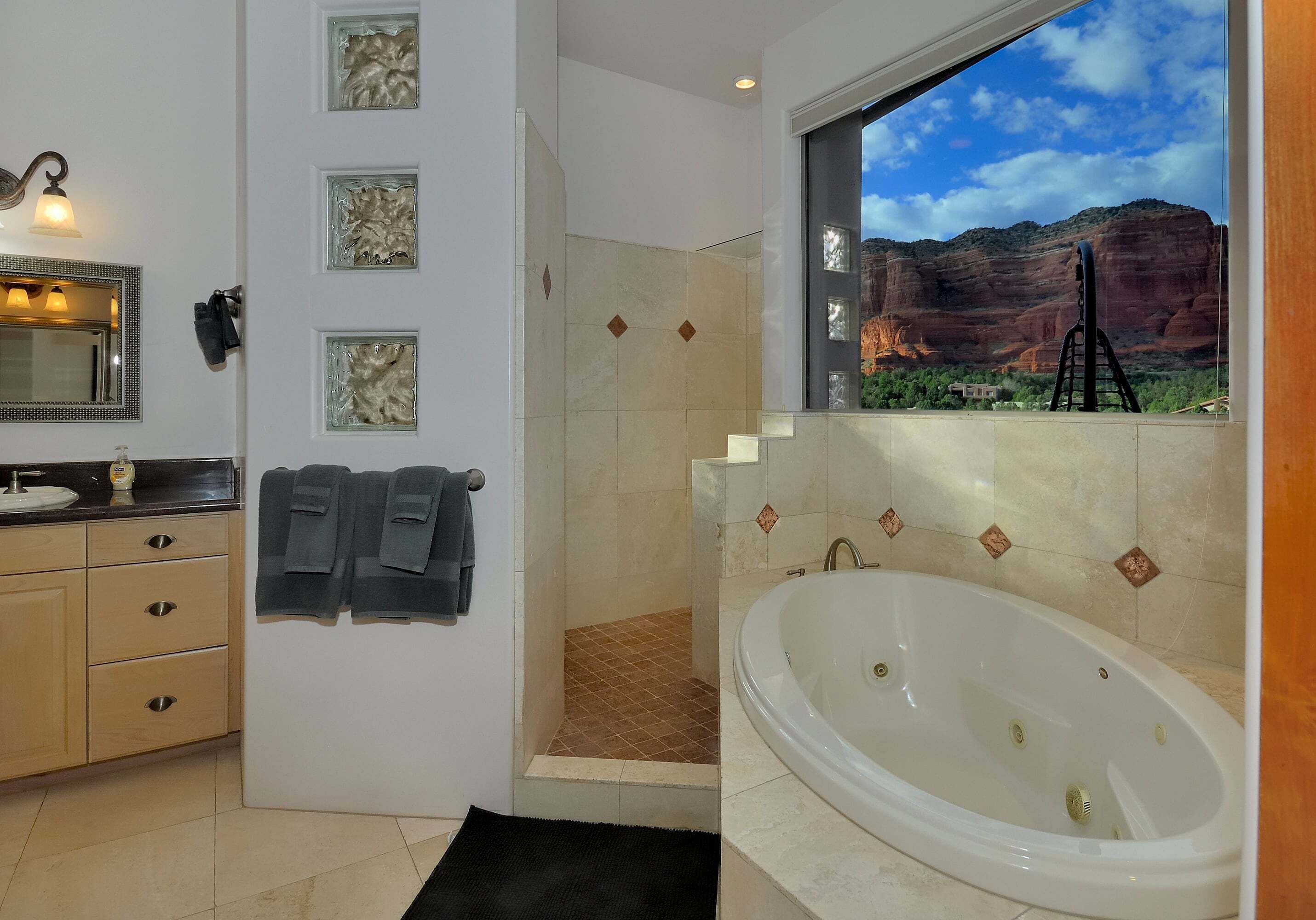 A bathroom with a large bathtub, a shower, a sink, and a mirror. There are towels hanging on the wall and a window with a view of a canyon.