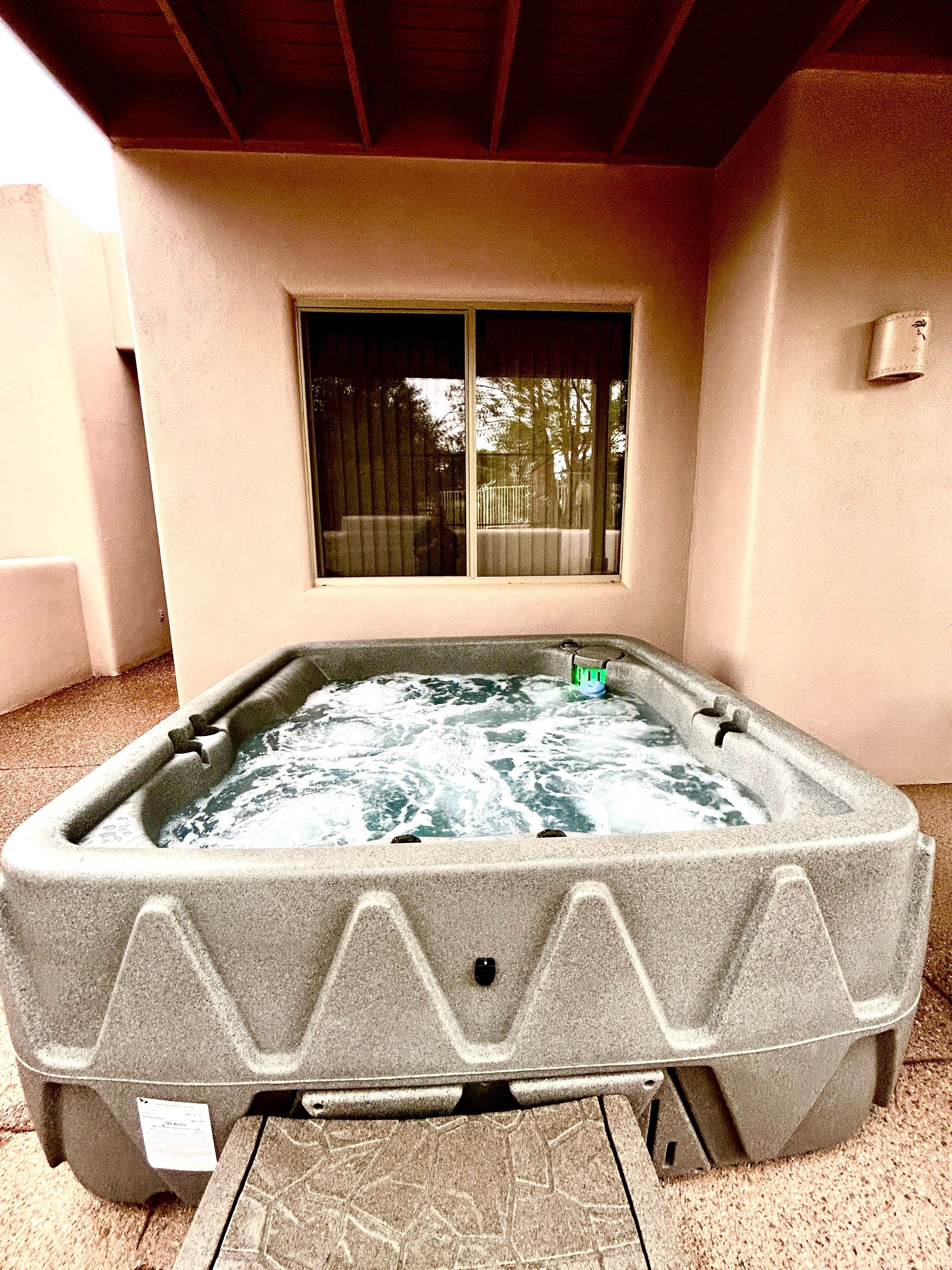 A hot tub in a covered outdoor area with a window above it.