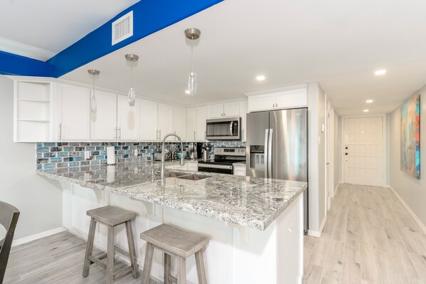 A modern kitchen with white cabinets, a granite island, stainless steel appliances, and pendant lighting.