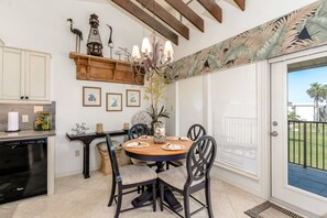 A dining area with a round table, chairs, a chandelier, and a view of the outdoors. - Sunchase Beachfront 205 - 2nd-Floor, Spacious Feel, Vaulted Ceilings, Wonderfully Appointed (South Padre Island)