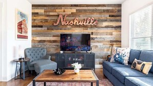A living room with a TV, a sofa, a coffee table, and a wall with a 'Nashville' sign.
